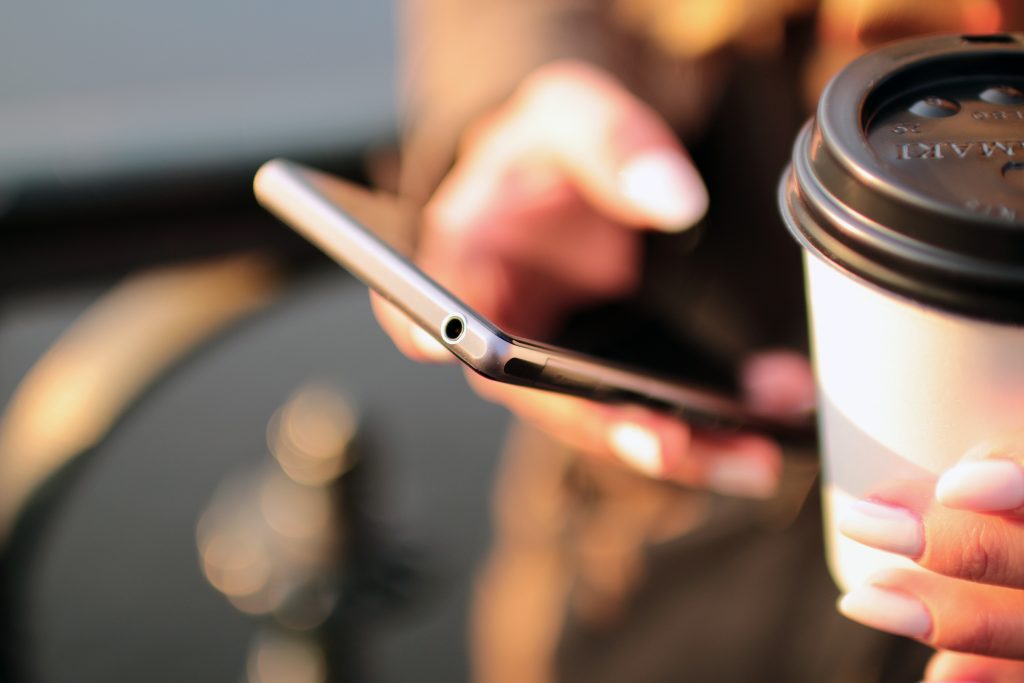 This is a picture of someone holding a cup of coffee and their phone.